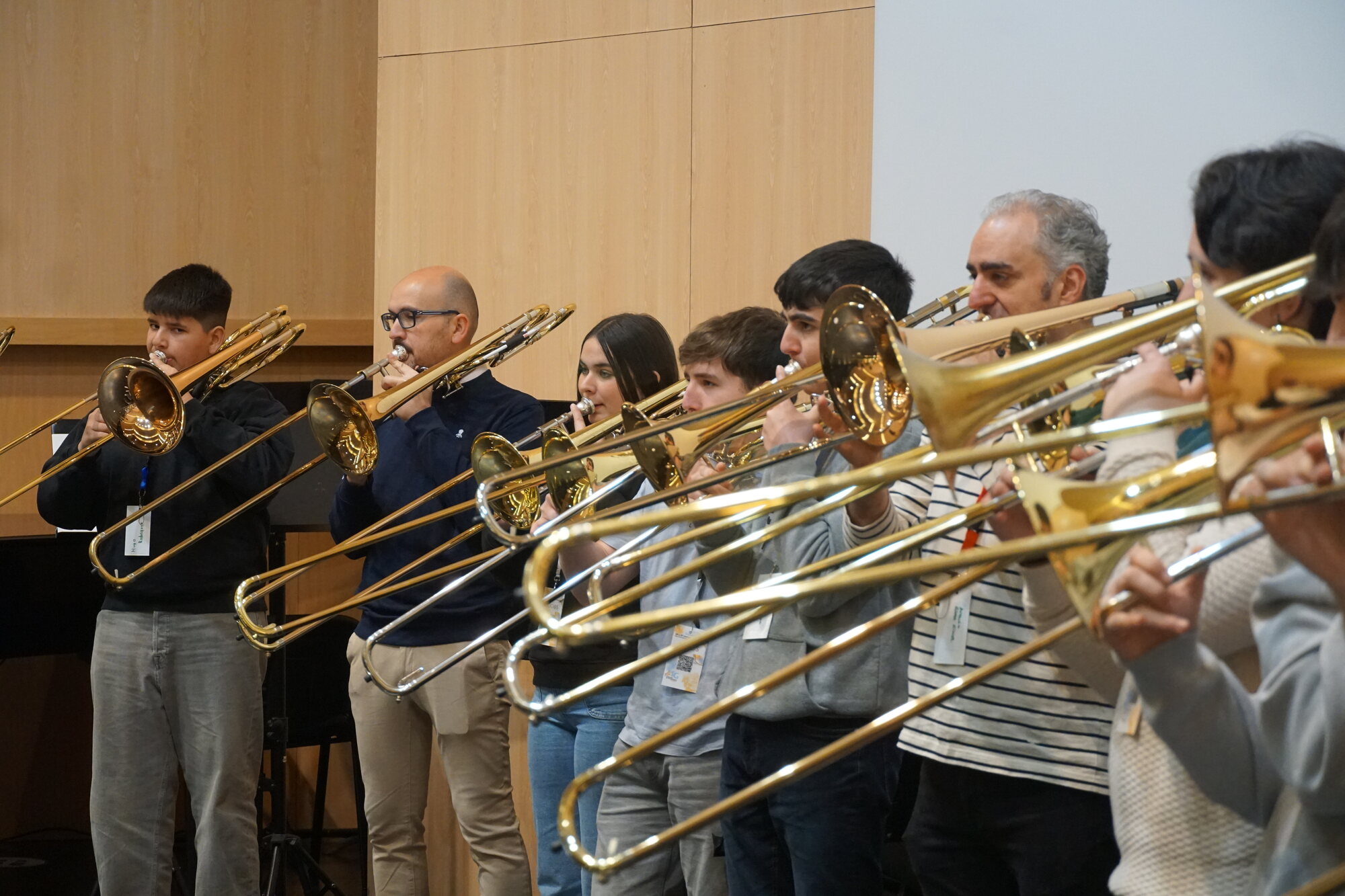 Trombonistas de todas as idades tocando en fila, vistos de perfil